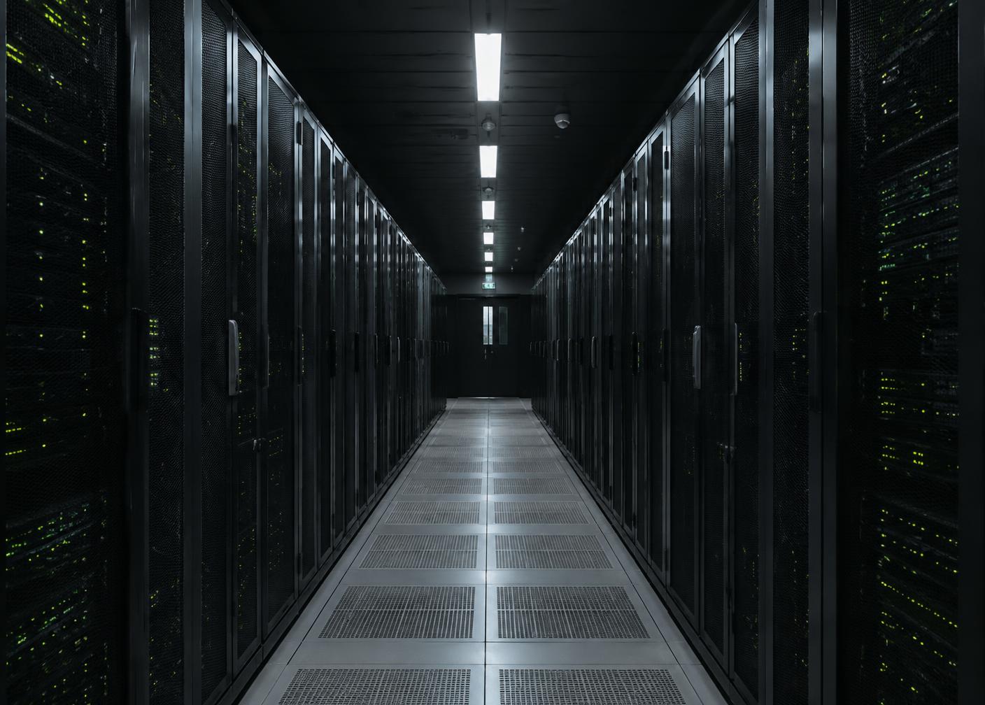 Long corridor of server racks in a dimly lit data centre with green status lights